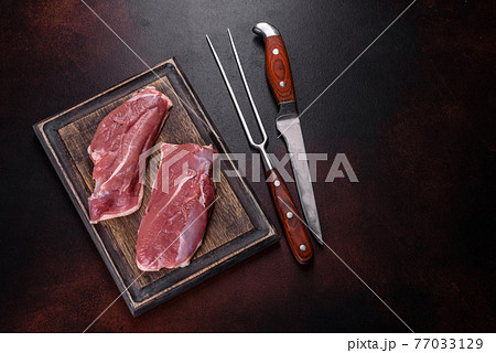 Raw duck breast with herbs and spices on a dark concrete background 77033129