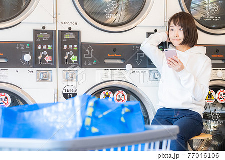 コインランドリーで洗濯を待っている女性 コインランドリーで洗濯を待っている女性 77046106