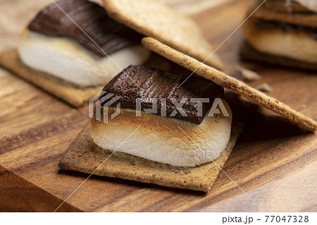 焼いたマシュマロとチョコレートをクラッカーに挟んだスモア 77047328