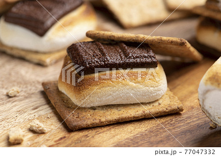 焼いたマシュマロとチョコレートをクラッカーに挟んだスモア 77047332