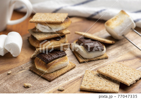 焼いたマシュマロとチョコレートをクラッカーに挟んだスモア 77047335