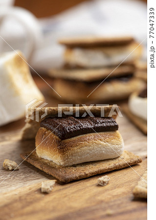 焼いたマシュマロとチョコレートをクラッカーに挟んだスモア 77047339