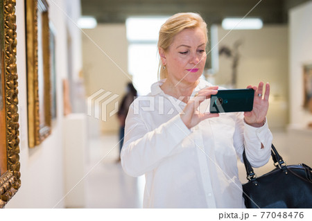 Female visitor taking picture in art gallery 77048476