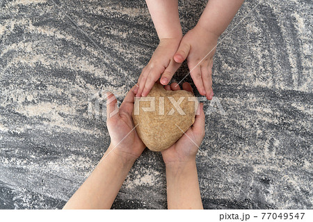 Childrens hands with dough over the table at home kitchen. Dough in shape of heart 77049547