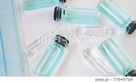 Vial vaccine, top view of glass ampoules with transparent and blue liquid lying on white background, global vaccination concept 77049789