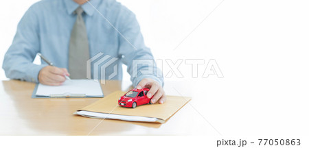 A Car on document envelope with man signing purchase documents in background. while hand complete the insurance policy, rental documents and loan document. concept guy buying new car 77050863