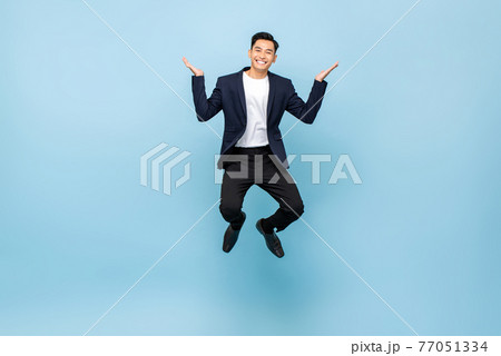 Happy Asian man jumping and smiling with open hands on isolated light blue studio background 77051334
