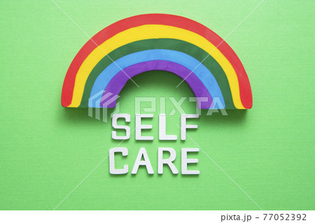 Self care word abstract quote on wooden blocks with rainbow over green background. 77052392