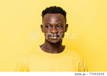 Close up portrait of young smiling African man looking away on isolated yellow studio background 77052630