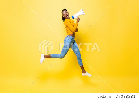 Jumping portrait of shocked young African American woman holding megaphone making announcement 77053531