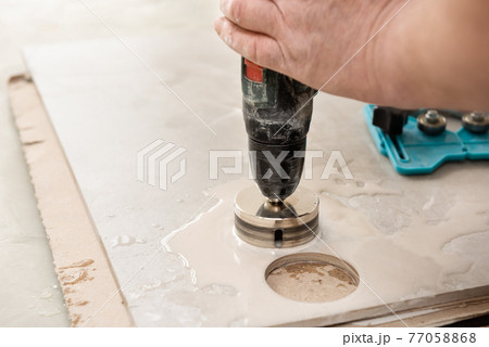 A tiler is using a diamond crown to drill holes in the ceramic tile. 77058868