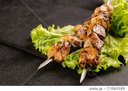 Two portions of shish kebab on a stone plate with salad. 77060389