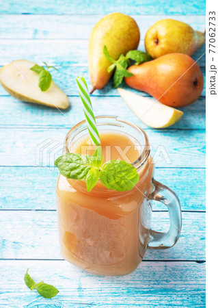 Natural pear juice in a glass cup. Juicy ripe conferences pears and mint leaves. Bright blue background. 77062733