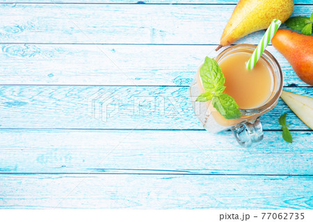 Natural pear juice in a glass cup. Juicy ripe conferences pears and mint leaves. top view copy space Bright blue background. 77062735