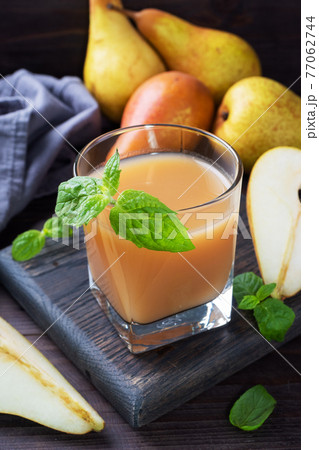 Natural pear juice in a glass cup. Juicy ripe conferences pears and mint leaves. Dark rustic wooden background. 77062744