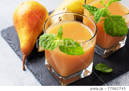 Natural pear juice in a glass cup. Juicy ripe conferences pears and mint leaves. Slate stand, light concrete background. 77062745
