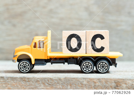 Toy truck hold alphabet letter block in word OC (Abbreviation of opportunity cost or original content, character) on wood background 77062926