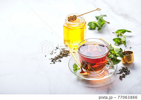 Black tea in glass transparent mug with mint leaves and honey. Calming and revitalizing tea, anti-stress and relaxation 77063866