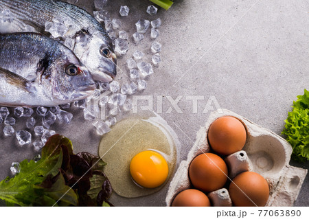 Frame of raw cooking ingredients for tasty and healthy food. Fresh dorado fish on ice, vegetables, eggs on gray concrete background top view. 77063890