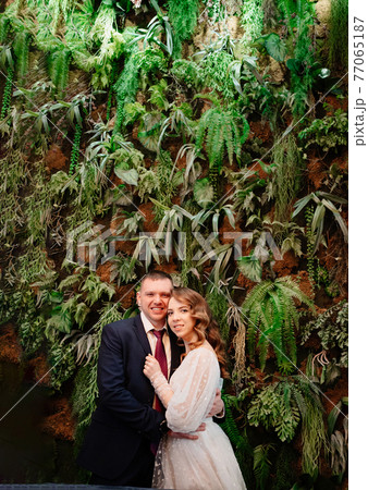 happy bride and groom at the wall decorated with live plants.  77065187