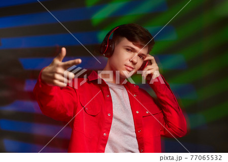 young man in red shirt with headphones listening to music young man in red shirt with headphones listening to music 77065532
