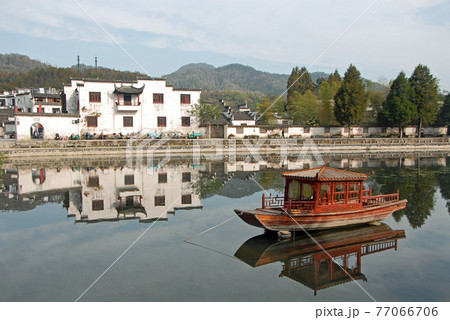 Xidi Ancient Town in Anhui Province, China. A house in the old town seen across Ming Jing Lake with boat. Ancient town of Xidi in China with old buildings, lake and trees in fall. 77066706