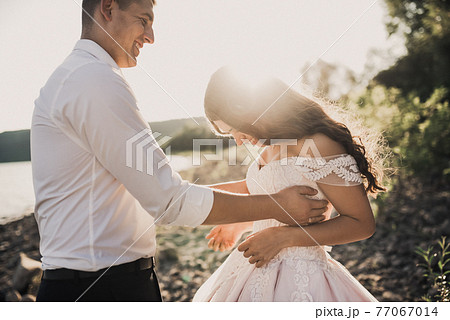 bride and groom laughing run together against rays of setting sun in summer  77067014