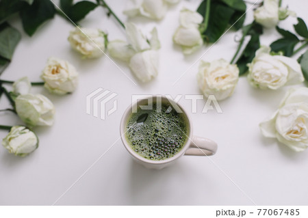 A cup of green matcha tea with white roses on white background view from above. Flatlay, top view, copy space 77067485
