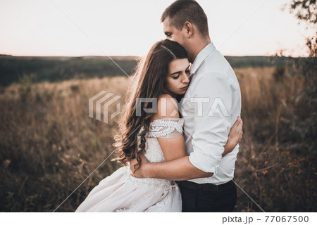 bride and groom walking on the meadow in summer at sunset bride and groom walking on the meadow in summer at sunset 77067500