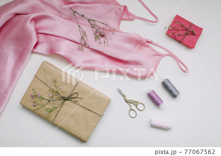 Composition with pink silk fabric, gift in craft paper and threads and scissors on white background. Flat lay, top view. Hobby, leisure concept. 77067562