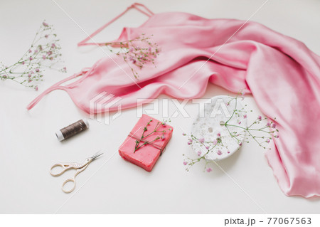 Composition with pink silk fabric, gift in craft paper and threads and scissors on white background. Flat lay, top view. Hobby, leisure concept. Composition with pink silk fabric, gift in craft paper and threads and scissors on white background. Flat lay, top view. Hobby, leisure concept. 77067563
