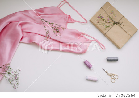 Composition with pink silk fabric, gift in craft paper and threads and scissors on white background. Flat lay, top view. Hobby, leisure concept. 77067564