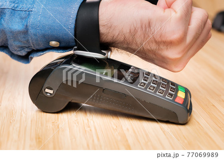 Customer paying through smartwatch using NFC technology. Contactless payment terminal machine. Customer paying through smartwatch using NFC technology. Contactless payment terminal machine. 77069989