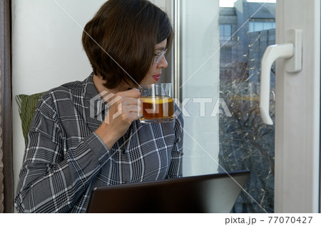 Attractive woman sit on windowsill with notebook and cup of tea 77070427