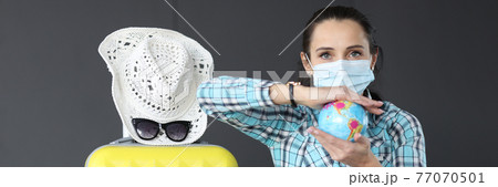 Woman in medical protective mask sits next to suitcase and holds globe with bacteria in her hand 77070501