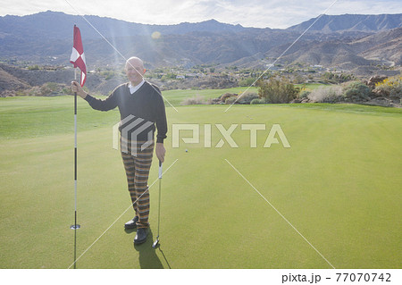 Full length portrait of happy senior male golfer holding flag and putter at golf course Full length portrait of happy senior male golfer holding flag and putter at golf course 77070742