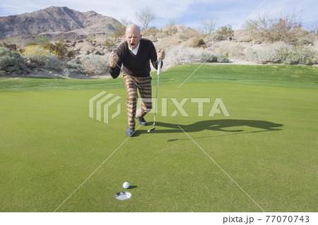 Full length of senior male golfer celebrating sinking putt at golf course Full length of senior male golfer celebrating sinking putt at golf course 77070743