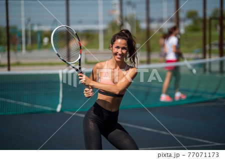 Sportive caucasian woman posing with a racket on a tennis court outdoors. 77071173