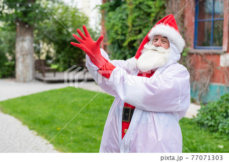 Santa claus in a protective costume puts on gloves. 77071303