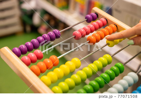 Closeup female hand calculating with balls on wooden rainbow abacus for number calculation. The concept of learning arithmetic for preschoolers. 77071508
