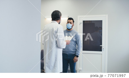 Male doctor speaking with patient in hospital hallway 77071997