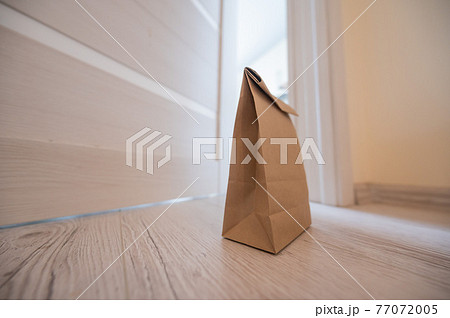 The concept of contactless delivery during the quarantine period. Kraft paper bag with online purchase at the open entrance door in case of danger of the spread of coronavirus. 77072005