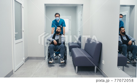 Handicapped male patient on wheelchair speaking with doctor in corridor Handicapped male patient on wheelchair speaking with doctor in corridor 77072058