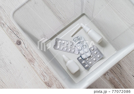 Medication in a white mesh metal wastebasket. Top view. Pills thrown into the trash. A paper basket with medicines inside on a wooden floor. Medication in a white mesh metal wastebasket. Top view. Pills thrown into the trash. A paper basket with medicines inside on a wooden floor. 77072086