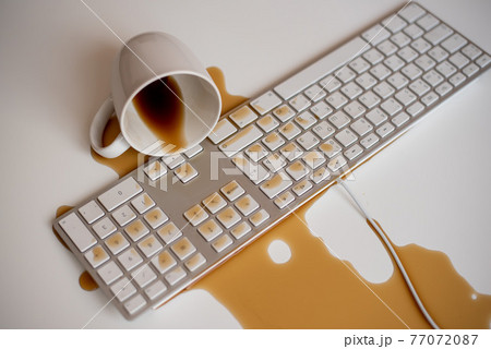 Spilled black coffee on a computer keyboard at a white table Spilled black coffee on a computer keyboard at a white table 77072087