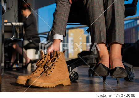 Business woman changes shoes with high heels on boots in the office. End of the working day. Tired legs Business woman changes shoes with high heels on boots in the office. End of the working day. Tired legs 77072089