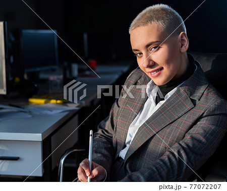 Serious young woman with short hair sits in armchair in office. 77072207