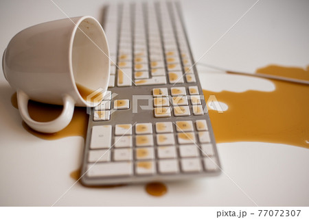 Spilled black coffee on a computer keyboard at a white table 77072307