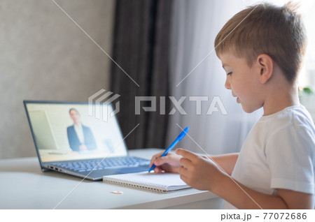 The boy communicates with a female teacher on a laptop webcam. Online lesson. Distance education in quarantine. A schoolboy is studying at home in the epidemic of coronavirus. 77072686