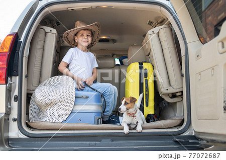 Happy boy in a cowboy hat and puppy jack russell terrier travel by car. A child and a funny little dog are sitting in the trunk and are ready for summer vacation. Independent travel. Best friends. Happy boy in a cowboy hat and puppy jack russell terrier travel by car. A child and a funny little dog are sitting in the trunk and are ready for summer vacation. Independent travel. Best friends. 77072687